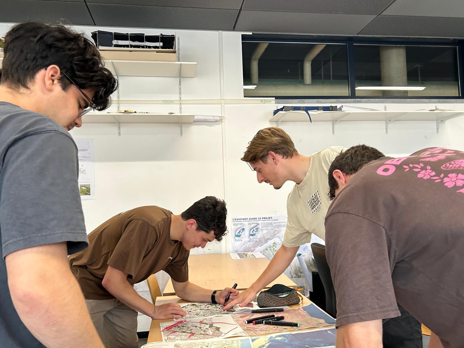 Séance de travail en atelier : Émile Pauchard et trois autres personnes annotent des plans étalés sur une table